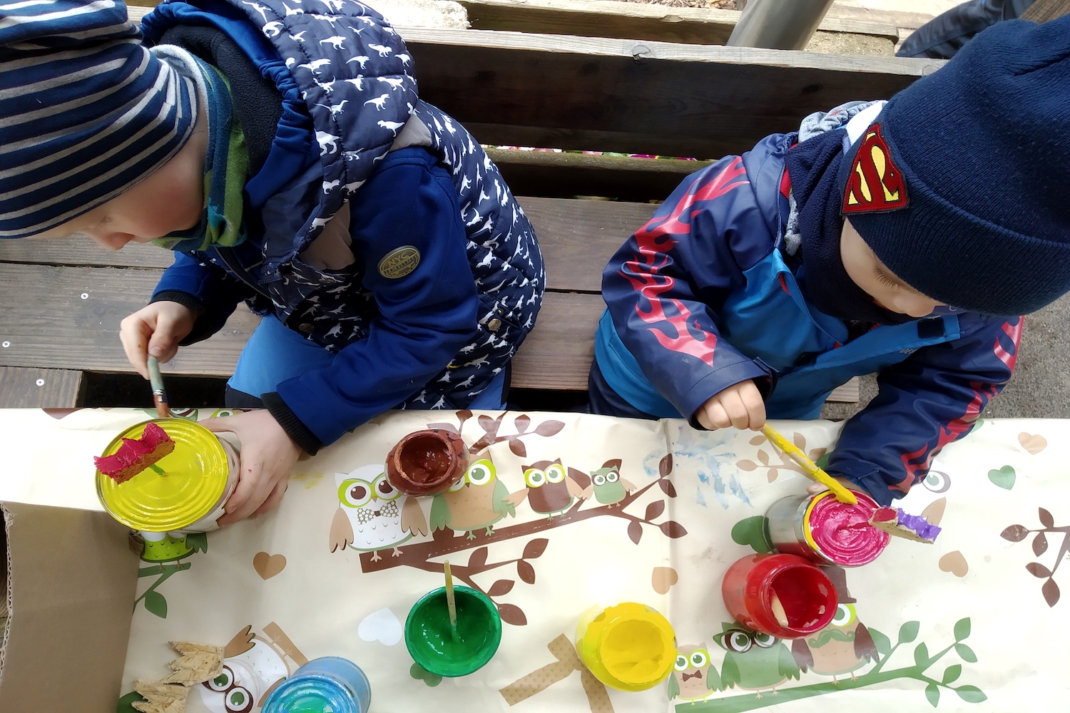 Naturkita Waldforscher - Zwei Kindergartenkinder auf einer Veranda bemalen mit Pinsel und Farben Blechdosen und Holzblumen.