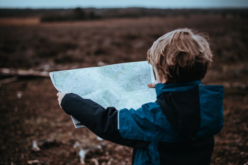 Naturkita Waldforscher - Ein Vorschulkind in einer braunen Herbstlandschaft hält mit beiden Händen eine Landkarte vor sich.