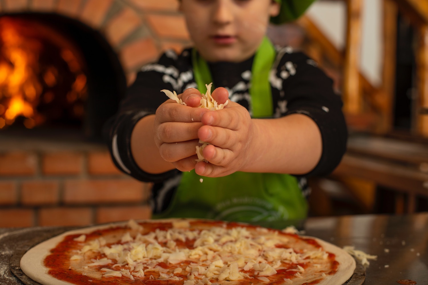 Gesunde Ernährung in der Naturkita - Für unsere Kinder nur das Beste. Die Kinder belegen ihre selbst gemachten Pizzen mit Käse und Gemüse.